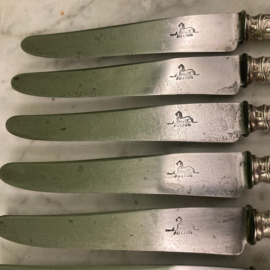 12 couteaux à entremets en métal argenté et lames acier. Modèle rubans croisés. Marque: Au Lion