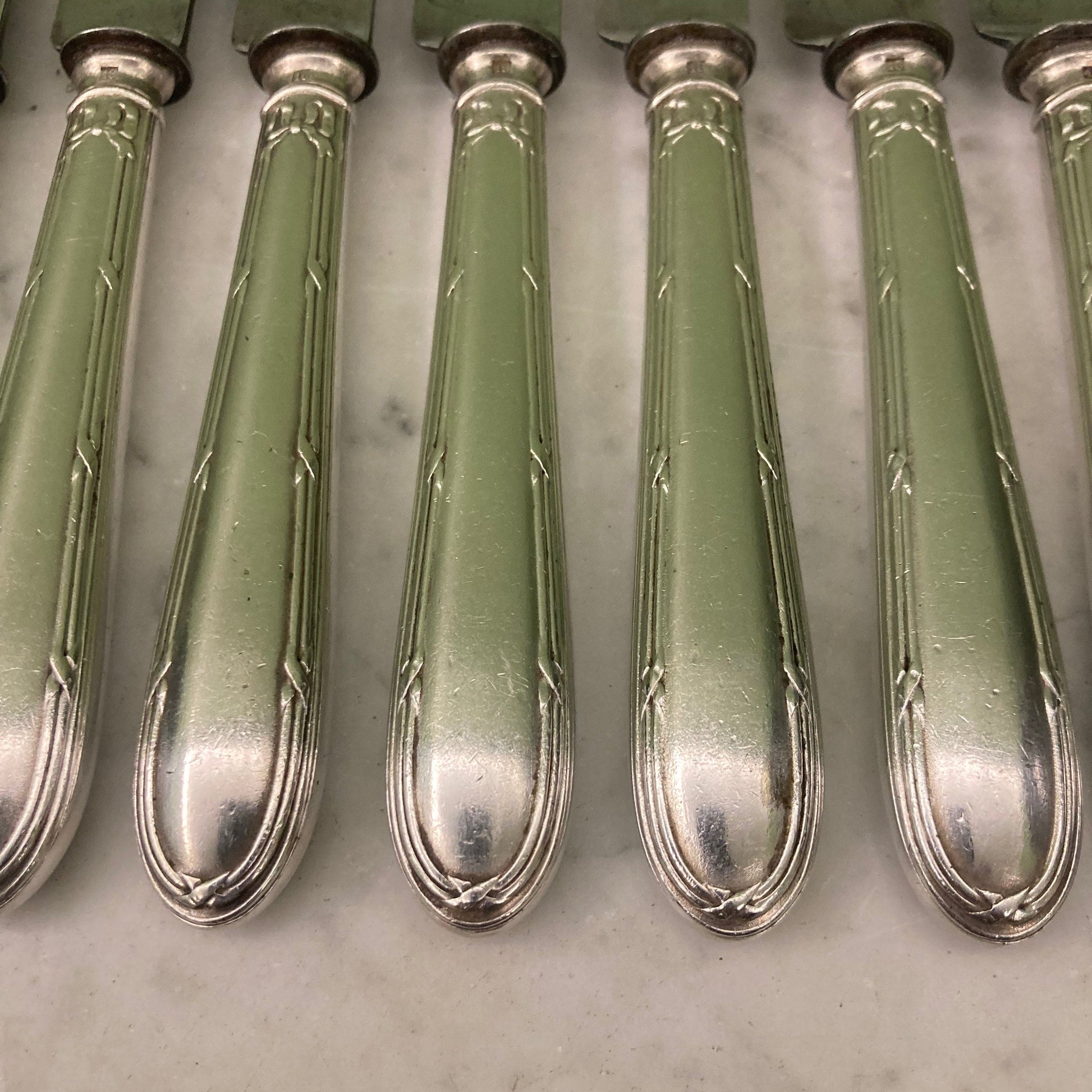 12 couteaux à entremets en métal argenté et lames acier. Modèle rubans croisés. Marque: Au Lion