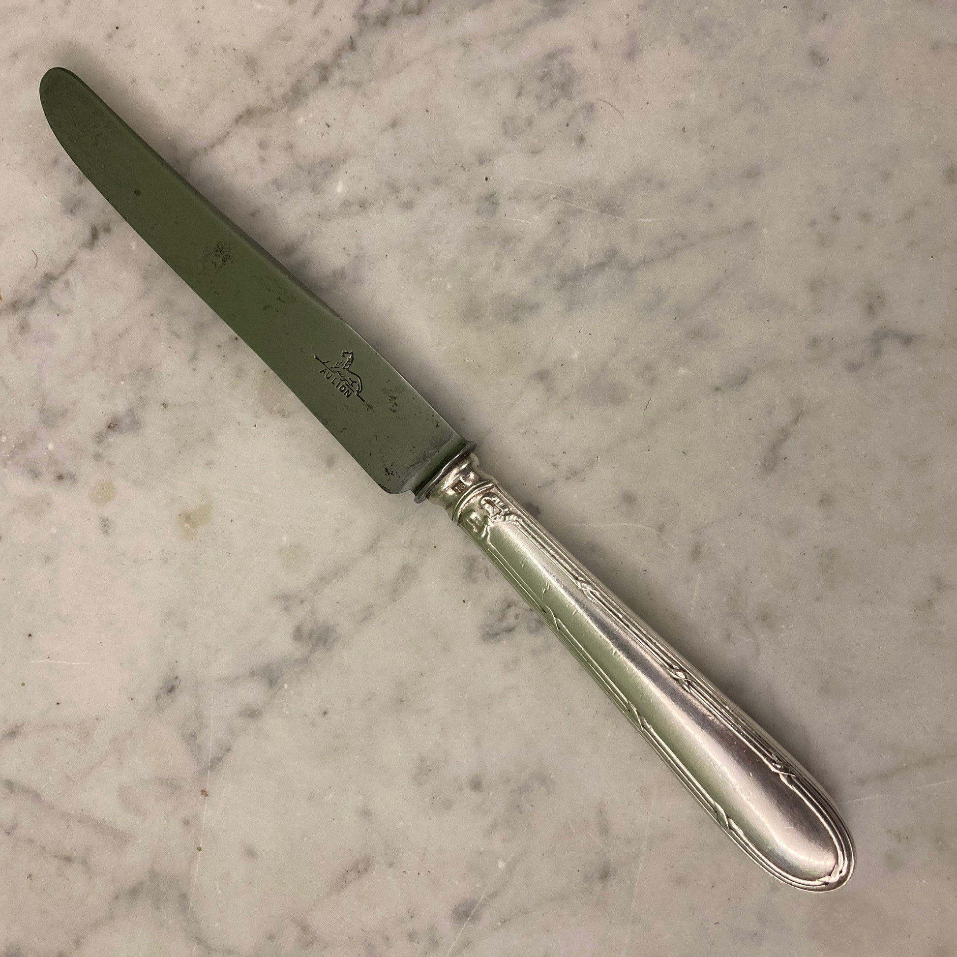 12 couteaux à entremets en métal argenté et lames acier. Modèle rubans croisés. Marque: Au Lion