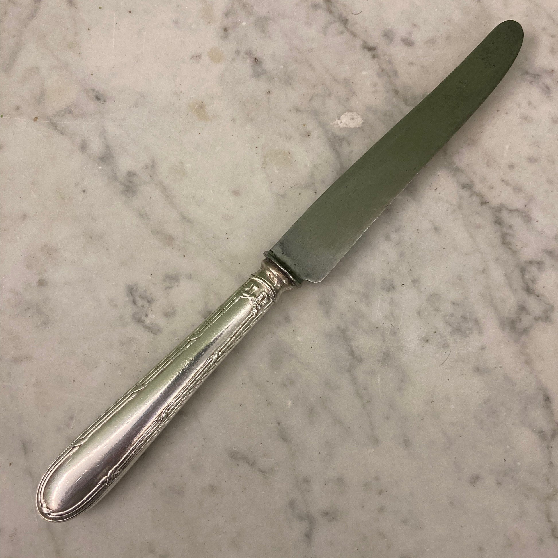 12 couteaux à entremets en métal argenté et lames acier. Modèle rubans croisés. Marque: Au Lion