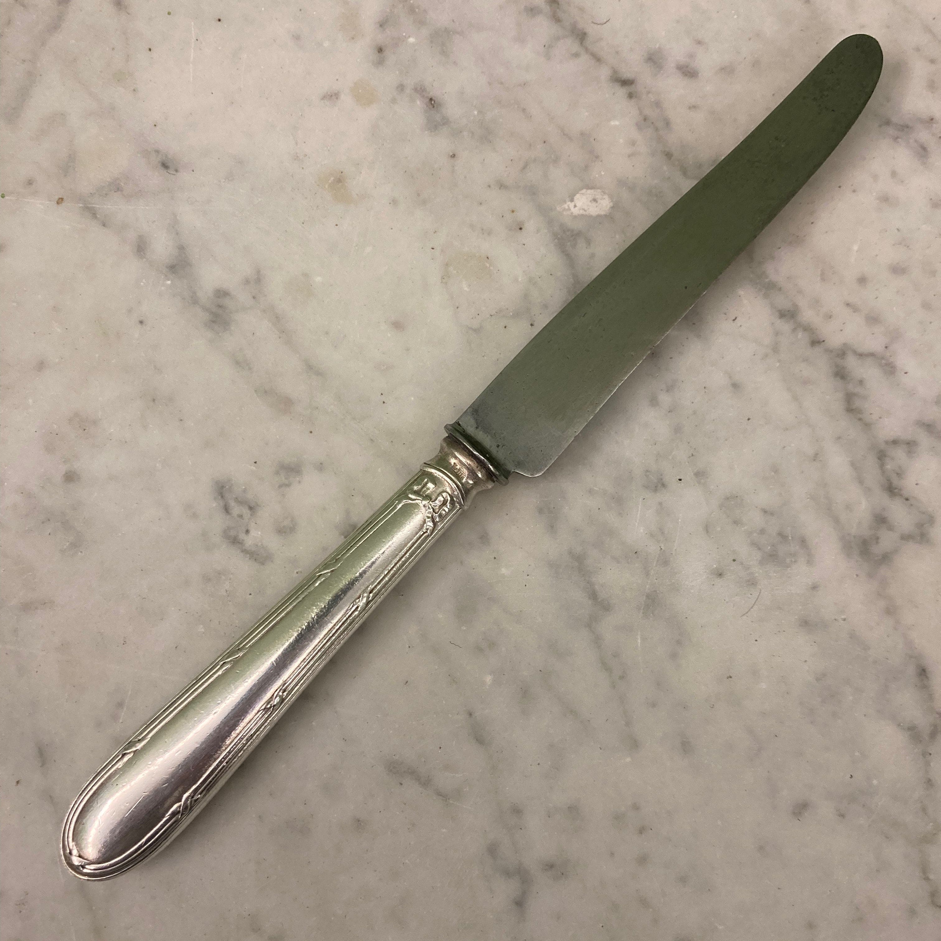 12 couteaux à entremets en métal argenté et lames acier. Modèle rubans croisés. Marque: Au Lion