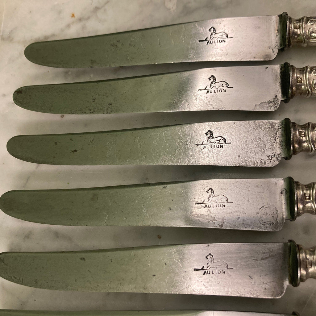 12 couteaux à entremets en métal argenté et lames acier. Modèle rubans croisés. Marque: Au Lion