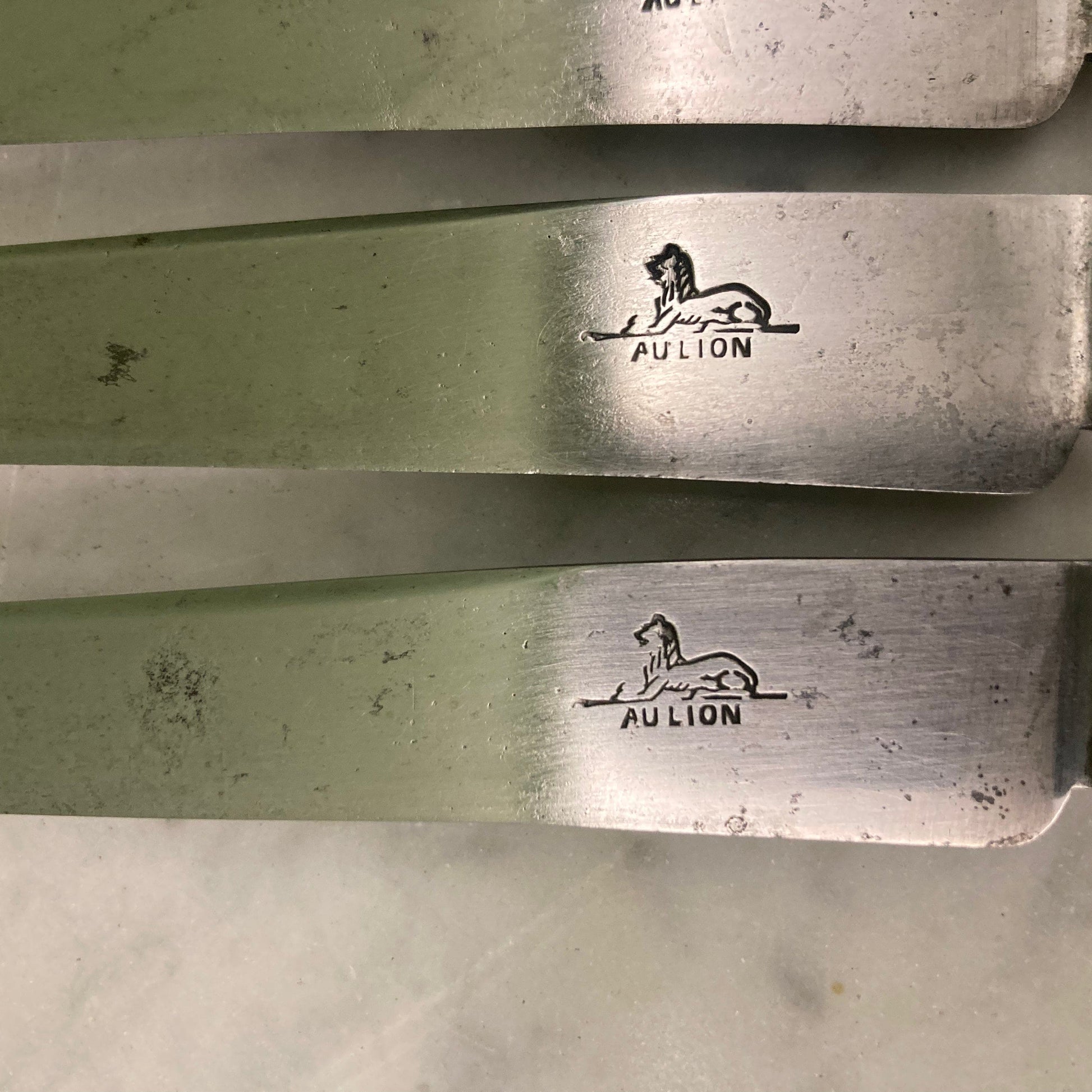 12 couteaux à entremets en métal argenté et lames acier. Modèle rubans croisés. Marque: Au Lion