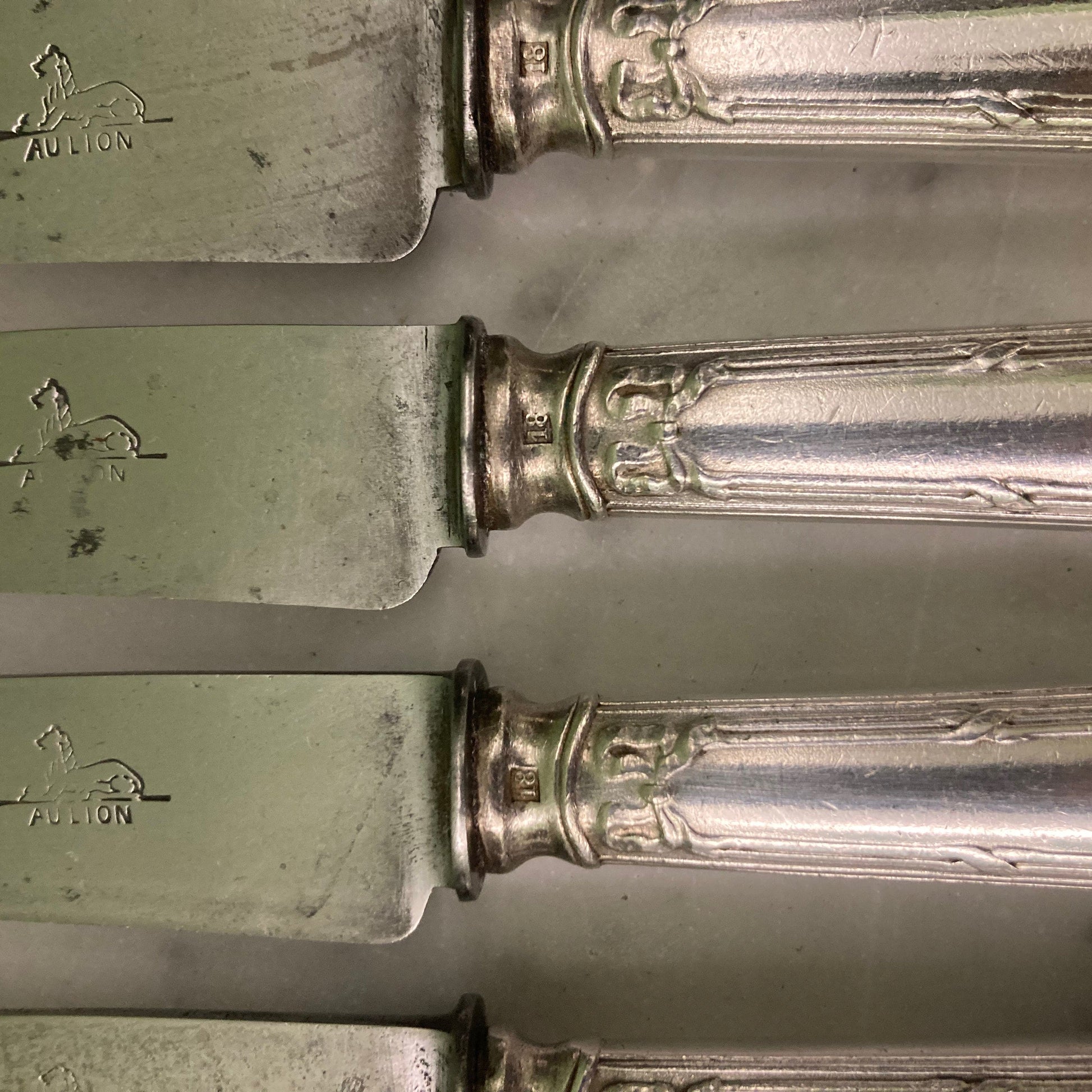 12 couteaux à entremets en métal argenté et lames acier. Modèle rubans croisés. Marque: Au Lion