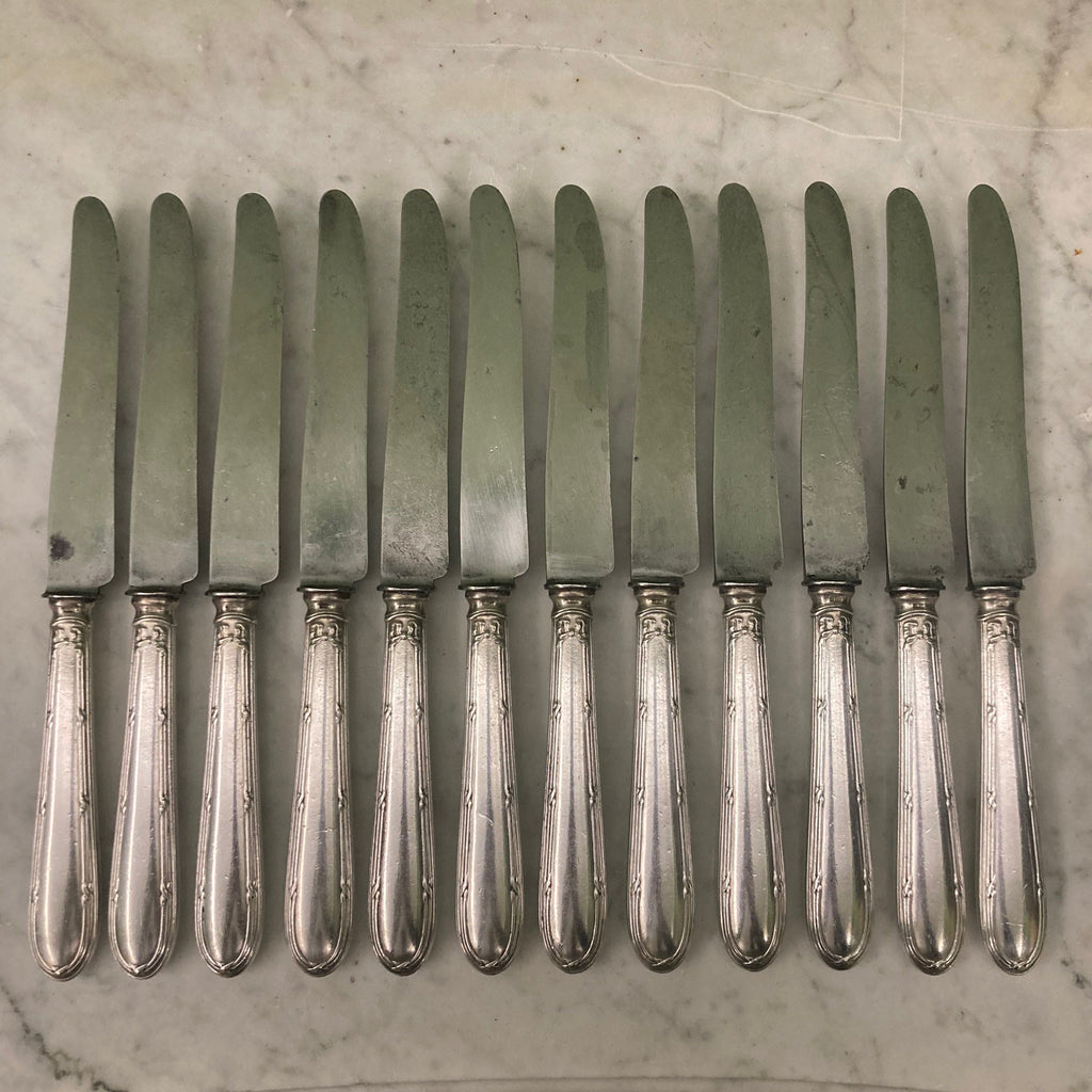 12 couteaux à entremets en métal argenté et lames acier. Modèle rubans croisés. Marque: Au Lion