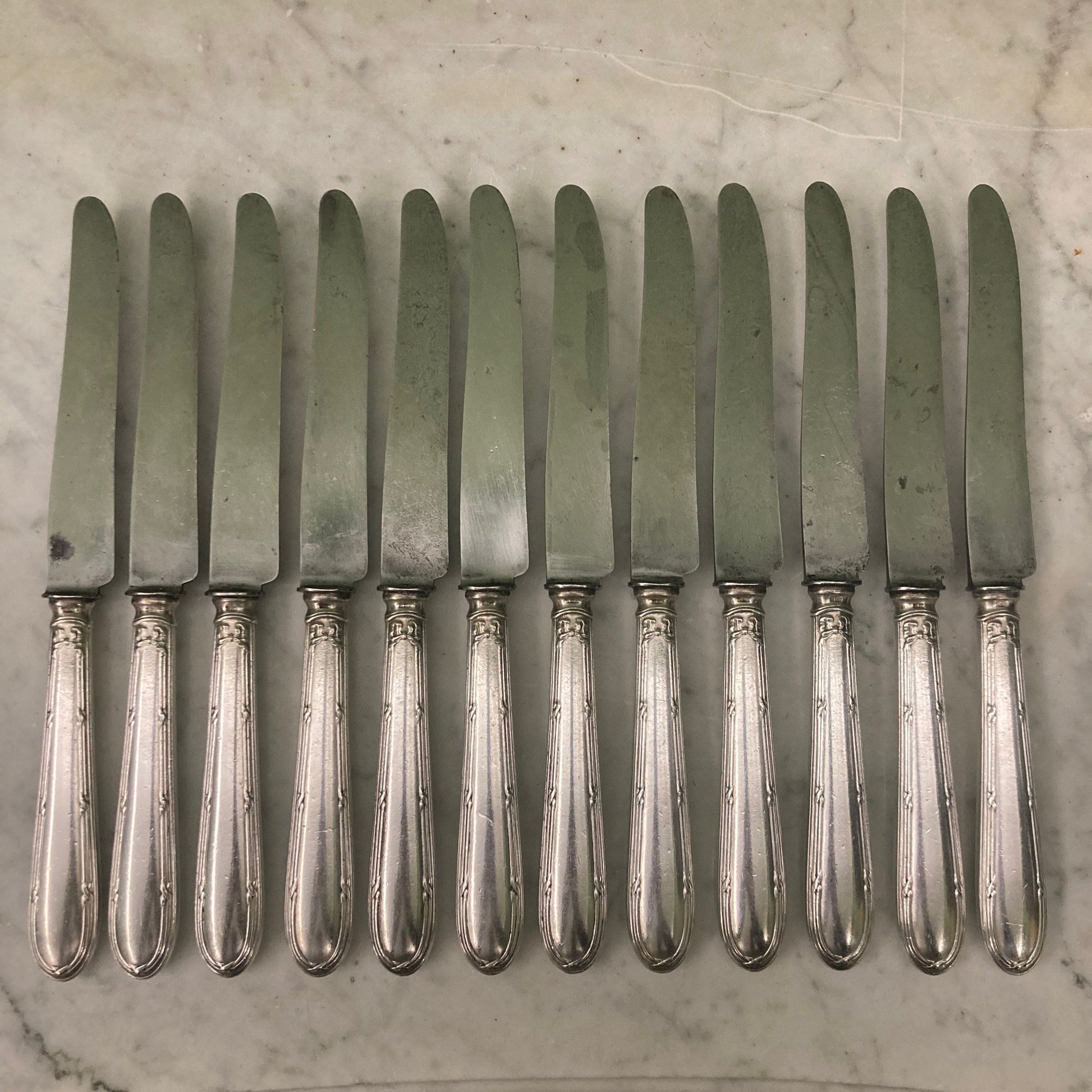 12 couteaux à entremets en métal argenté et lames acier. Modèle rubans croisés. Marque: Au Lion