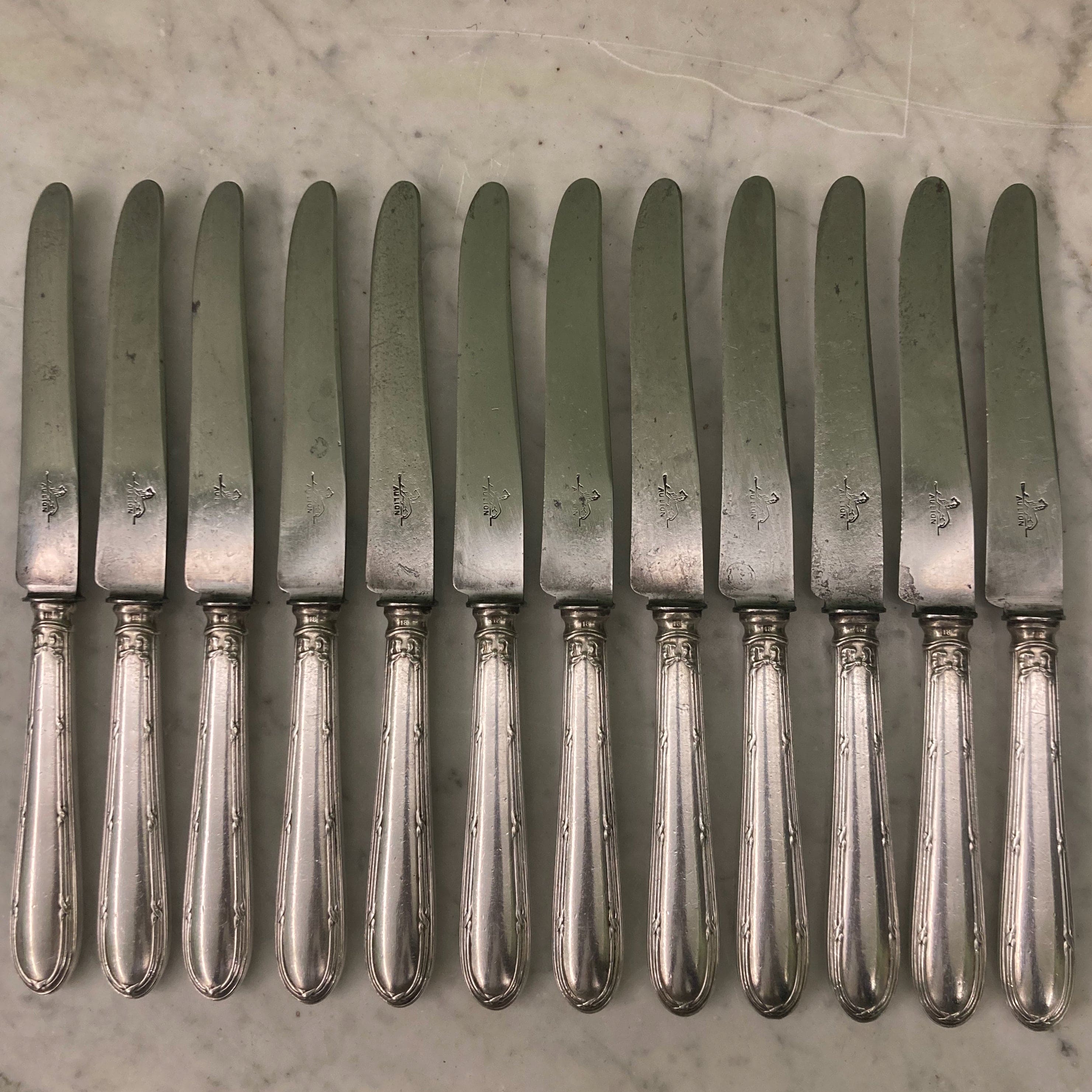 12 couteaux à entremets en métal argenté et lames acier. Modèle rubans croisés. Marque: Au Lion