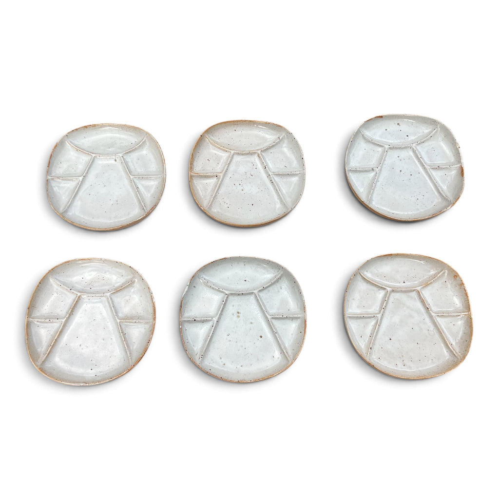 Vue de face de six assiettes a fondue compartimentées en céramique de Vallauris. Le modele présente un design géométrique épuré avec un email blanc crème satiné laissant apparaitre la terre cuite rousse sur les arreèes et la bordure extérieure.