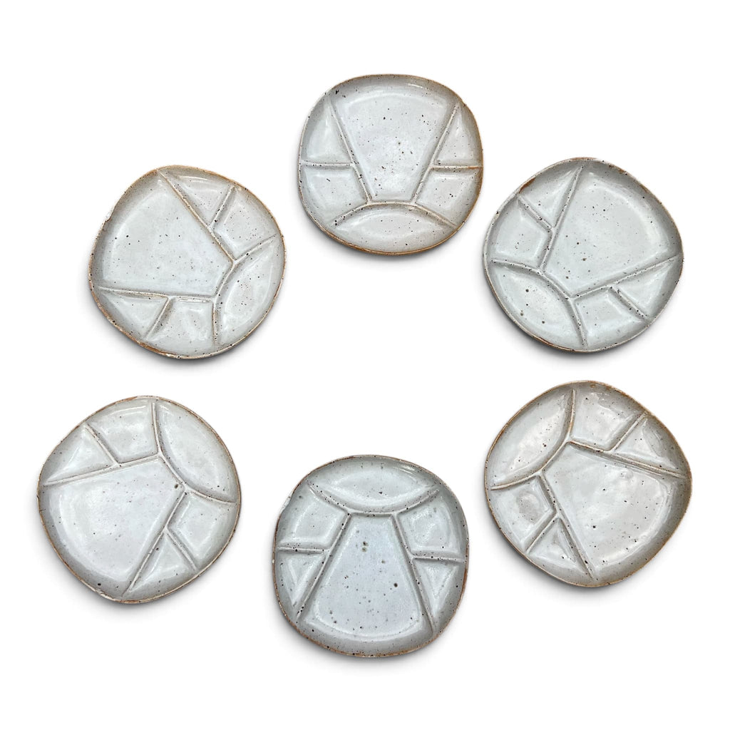 Vue de face de six assiettes a fondue compartimentées en céramique de Vallauris. Le modele présente un design géométrique épuré avec un email blanc crème satiné laissant apparaitre la terre cuite rousse sur les arreèes et la bordure extérieure.