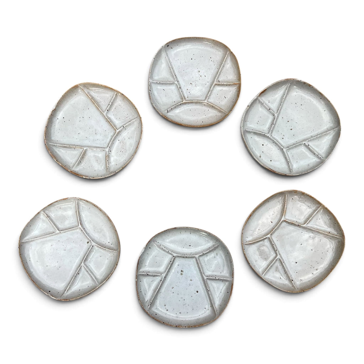 Vue de face de six assiettes a fondue compartimentées en céramique de Vallauris. Le modele présente un design géométrique épuré avec un email blanc crème satiné laissant apparaitre la terre cuite rousse sur les arreèes et la bordure extérieure.