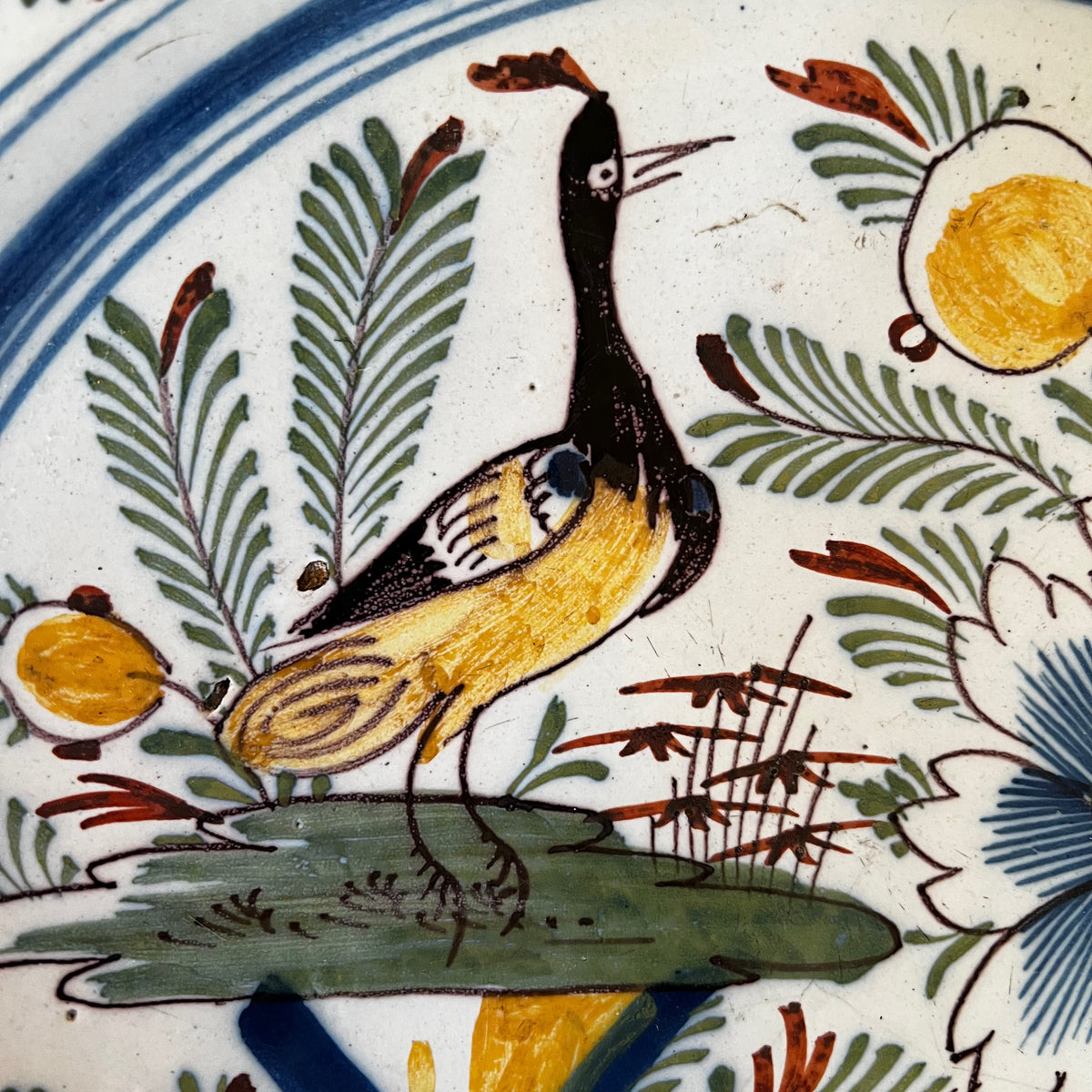 Détail peint à la main du décor sinisant représentant un oiseau exotique posé sur un tertre à côté d'une barrière jaune et bleue.
