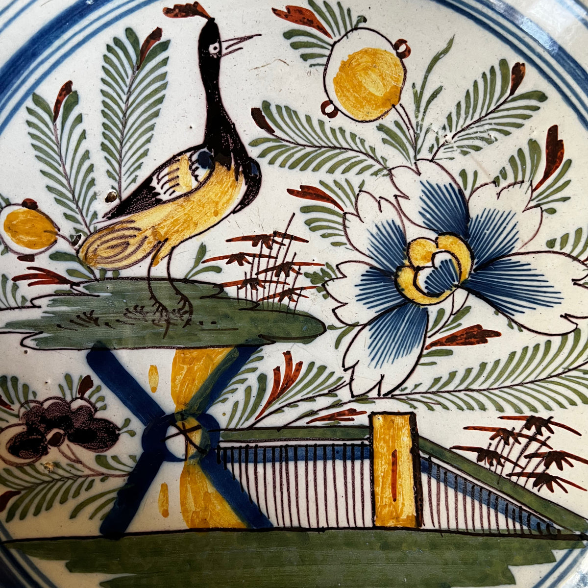 Détail peint à la main du décor sinisant représentant un oiseau exotique posé sur un tertre à côté d'une barrière jaune et bleue.

