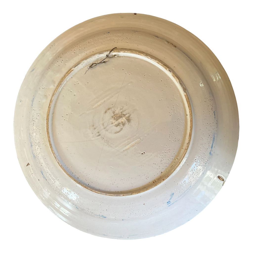 Revers du plat en faïence montrant la pâte calcaire très claire sous les égrenures d'usage de la bordure.
