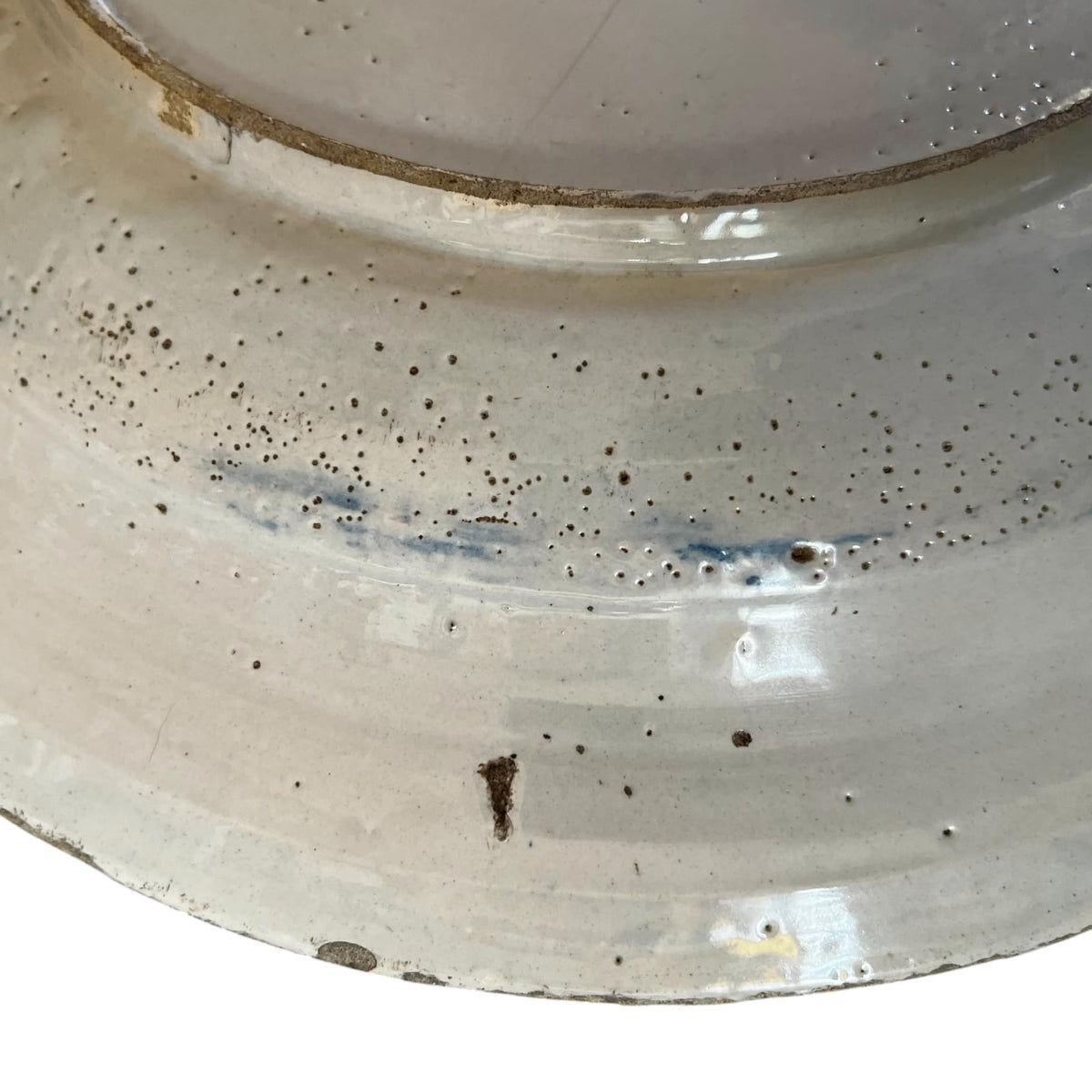 Revers du plat en faïence montrant la pâte calcaire très claire sous les égrenures d'usage de la bordure.
